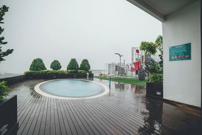 A rooftop pool area with a wooden deck, a circular pool, and a view of the cityscape.