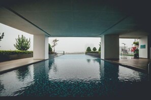 A modern indoor swimming pool with a clear view of the surrounding greenery and buildings. - Marina Residence 3BR Shores Haven nr Midvalley CIQ (Plentong)