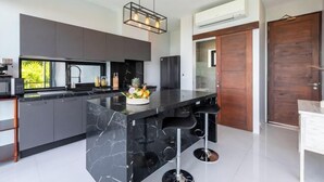 A modern kitchen with a marble island, bar stools, and a hanging light fixture. - L'Esterel Villa - A Tropical Oasis at Maenam Hills (Koh Samui)