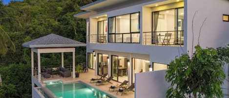 A modern two-story house with a swimming pool, outdoor seating, and a covered patio.