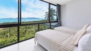 A bedroom with a large window, a bed with striped bedding, and a view of a tropical landscape. - L'Esterel Villa - A Tropical Oasis at Maenam Hills (Koh Samui)