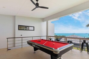 A pool table with a red felt surface, a ceiling fan, and a balcony with a view of the ocean. - L'Esterel Villa - A Tropical Oasis at Maenam Hills (Koh Samui)