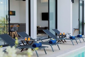 Zona junto a la piscina con sillones de descanso y una mesa con bebidas.