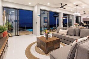 A modern living room with a sofa, coffee table, and a view of a pool. - L'Esterel Villa - A Tropical Oasis at Maenam Hills (Koh Samui)
