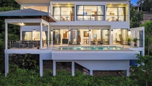 A modern two-story house with a large swimming pool, multiple balconies, and a covered outdoor seating area. - L'Esterel Villa - A Tropical Oasis at Maenam Hills (Koh Samui)