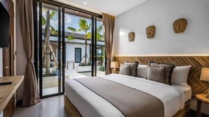 A modern hotel room with a large bed, a TV, and a view of palm trees through the sliding glass door.