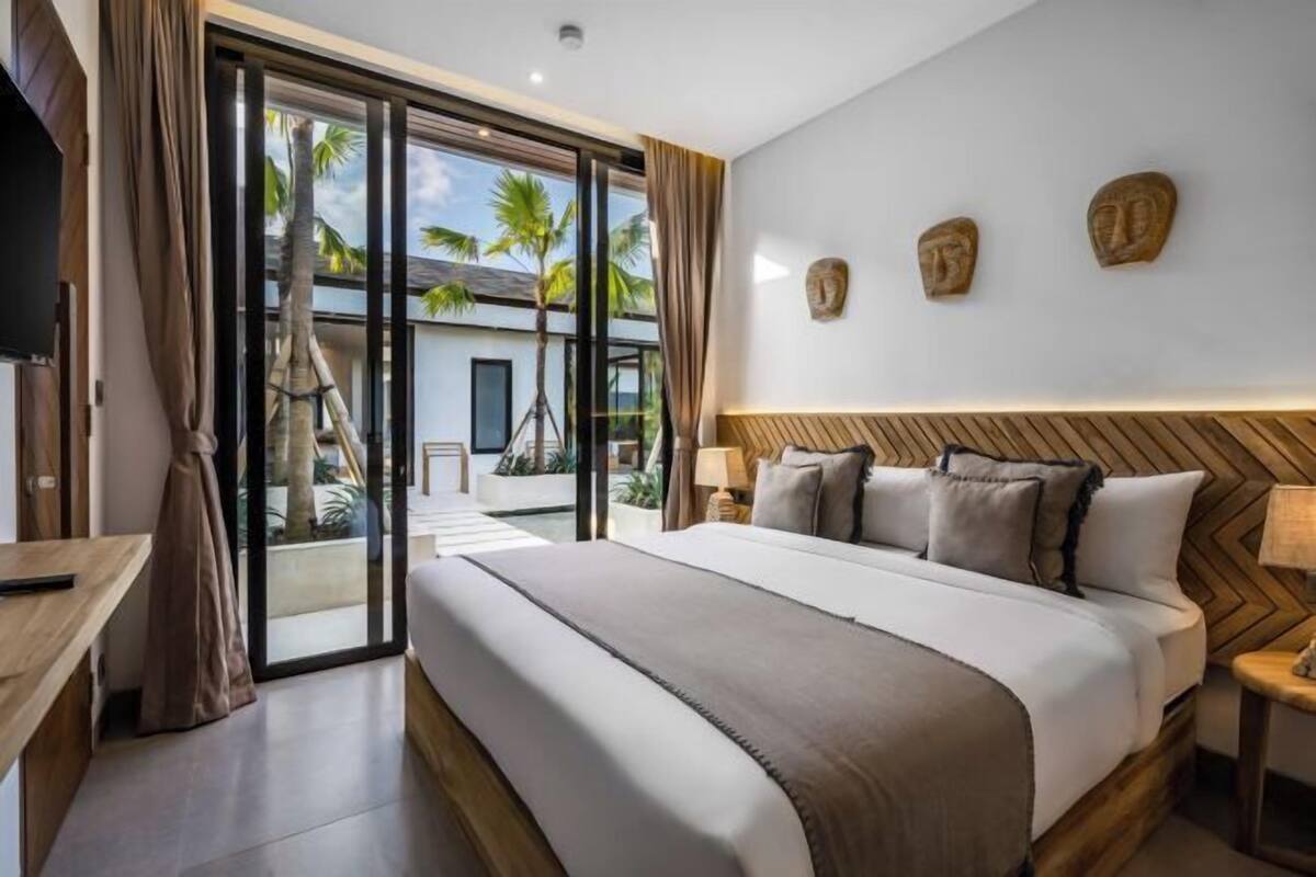 A modern hotel room with a large bed, a TV, and a view of palm trees through the sliding glass door.