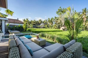 A modern outdoor lounge area with a pool, surrounded by lush greenery and palm trees. - Villa Juke by BaliSuperHost (Bali)