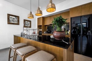 A modern kitchen with a central island, wooden cabinets, pendant lighting, and a large potted plant. - Villa Juke by BaliSuperHost (Bali)