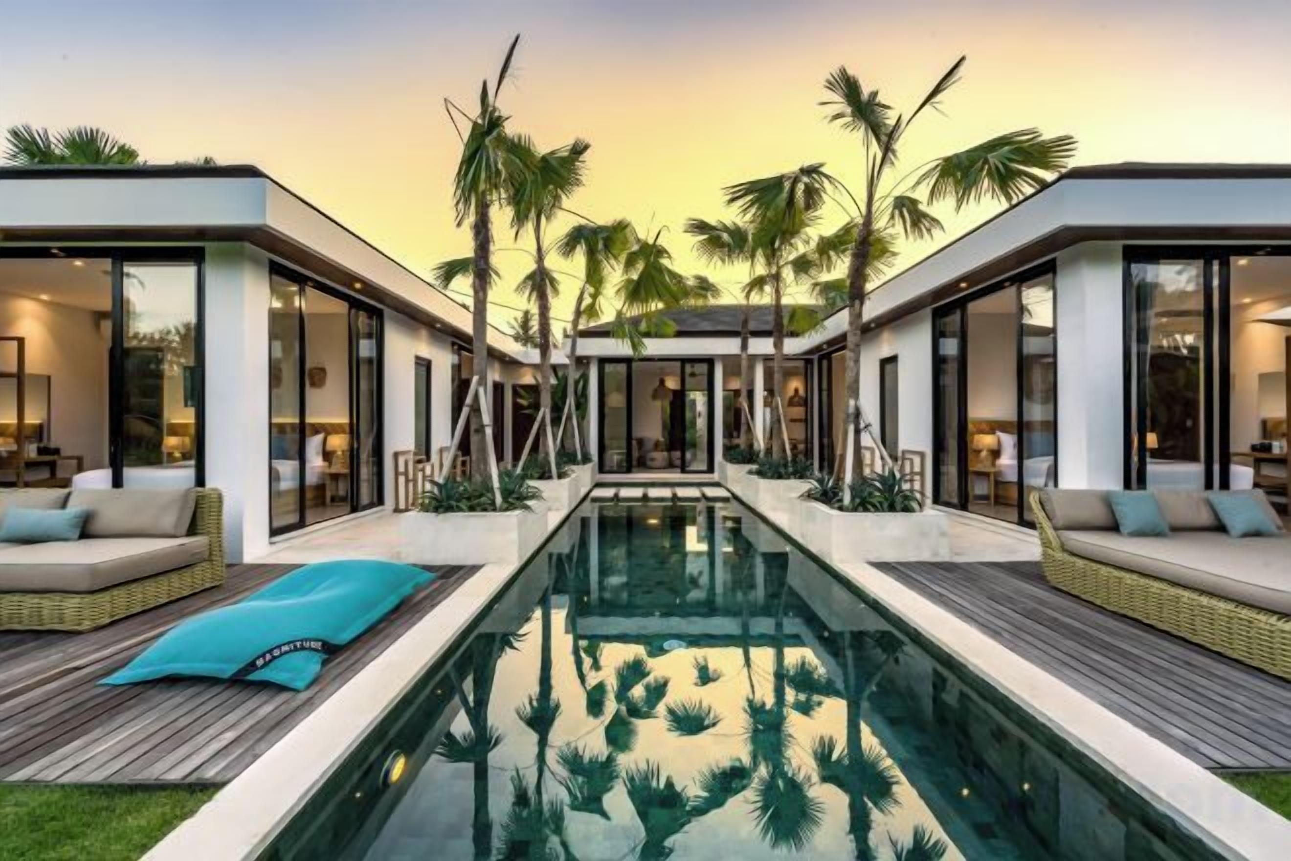 A modern poolside area with a clear pool, outdoor seating, and palm trees.