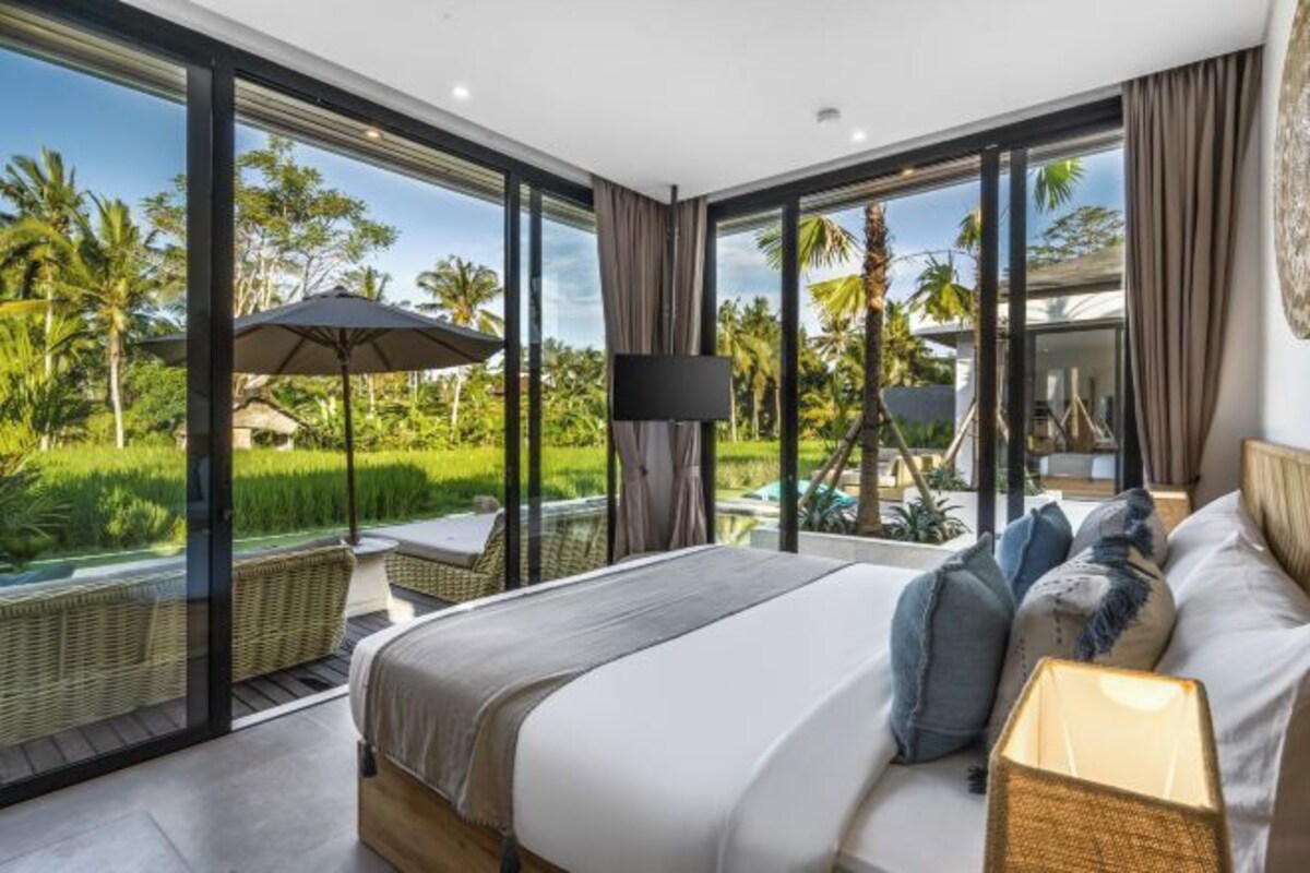 A modern bedroom with a large bed, a TV, and a view of a lush garden.