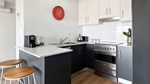 A modern kitchen with white cabinets, a stainless steel stove, and a red clock on the wall. - Beachside Breakaway Glenelg South – 200m to the Beach (Glenelg South)