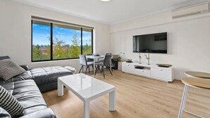 A modern living room with a sofa, coffee table, dining area, and a TV mounted on the wall. - Beachside Breakaway Glenelg South – 200m to the Beach (Glenelg South)