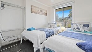 A bedroom with two beds, a window with a view, a ceiling fan, and a metal-framed chair. - Beachside Breakaway Glenelg South – 200m to the Beach (Glenelg South)