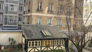 A small, traditional house with a sloped roof, surrounded by potted plants and a tree.