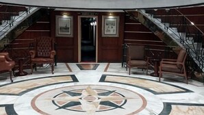 Eine Lobby mit einem zentralen, runden Marmorboden, einer imposanten Treppe und Ledersesseln.