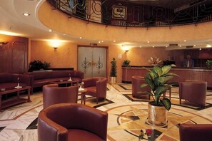 Una hall con una scalinata a forma di curva, una reception, posti a sedere in pelle e una grande pianta in vaso.