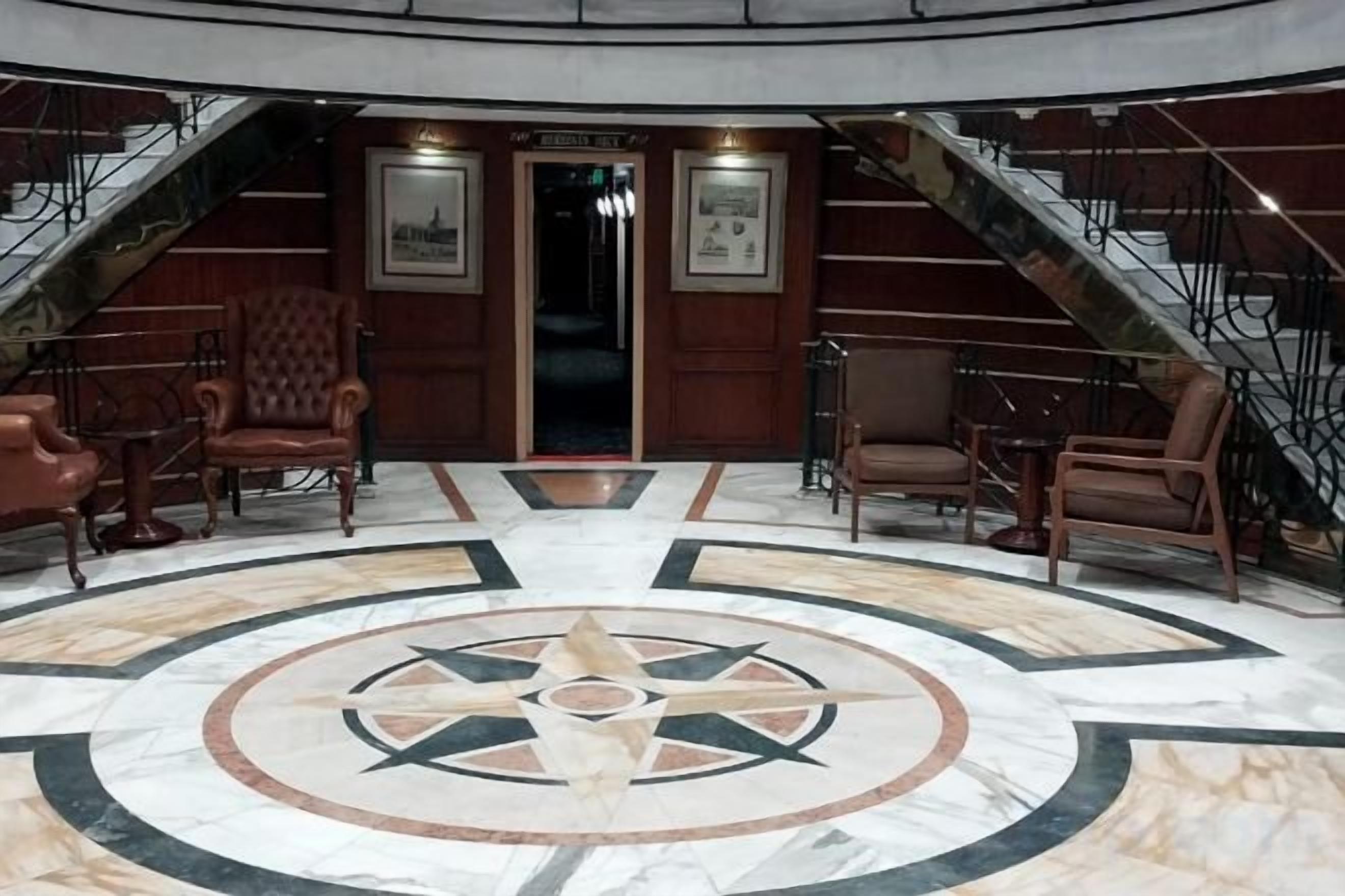 A lobby with a central circular floor design, a staircase, and seating areas.