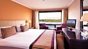 A hotel room with a bed, a desk, a television, and a view of a body of water. - Jaz Crown Prince Nile Cruise - Every Monday from Luxor for 07 & 04 Nights (At Tod)