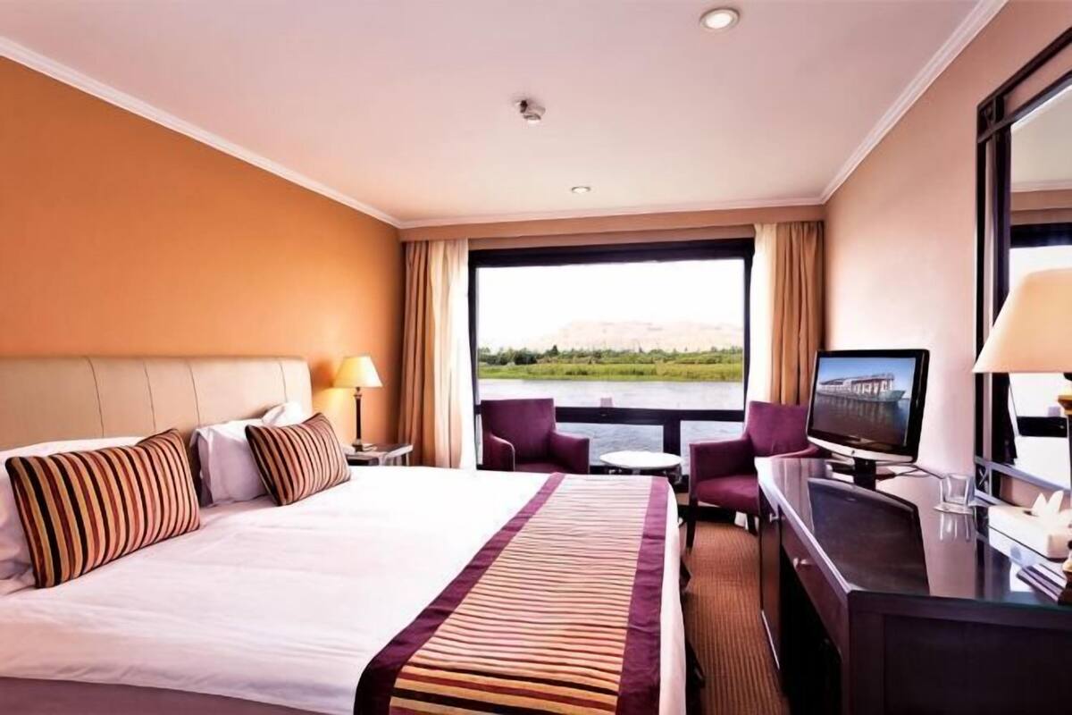 A hotel room with a bed, a desk, a television, and a view of a body of water.