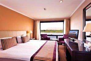 Ett hotellrum med en säng, ett skrivbord, en tv och utsikt över en vattenyta.