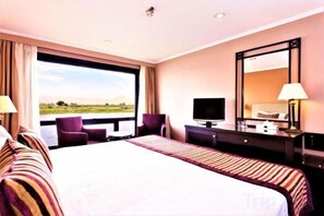 A hotel room with a large bed, a desk with a TV, a chair, and a view of the outdoors. - Jaz Crown Prince Nile Cruise - Every Monday from Luxor for 07 & 04 Nights (At Tod)