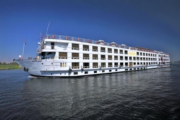 A large riverboat with multiple decks, a flag at the bow, and a clear sky.