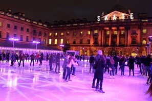 An outdoor ice skating rink with people skating, in front of a building with 'SAKAE' illuminated on the facade. - Eldon Chambers Pod 7 by City Living London (London)