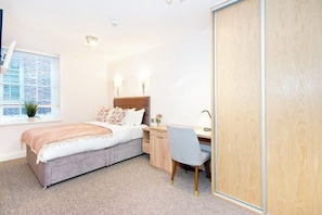 Een slaapkamer met een bed, bureau, stoel en een raam met jaloezieën.
