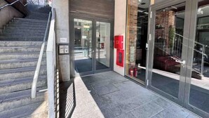 Une entrée moderne avec une porte en verre, un escalier et un extincteur fixé au mur.