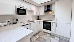 Une cuisine moderne avec des meubles blancs, un four encastré, un four à micro-ondes et un lave-vaisselle.
