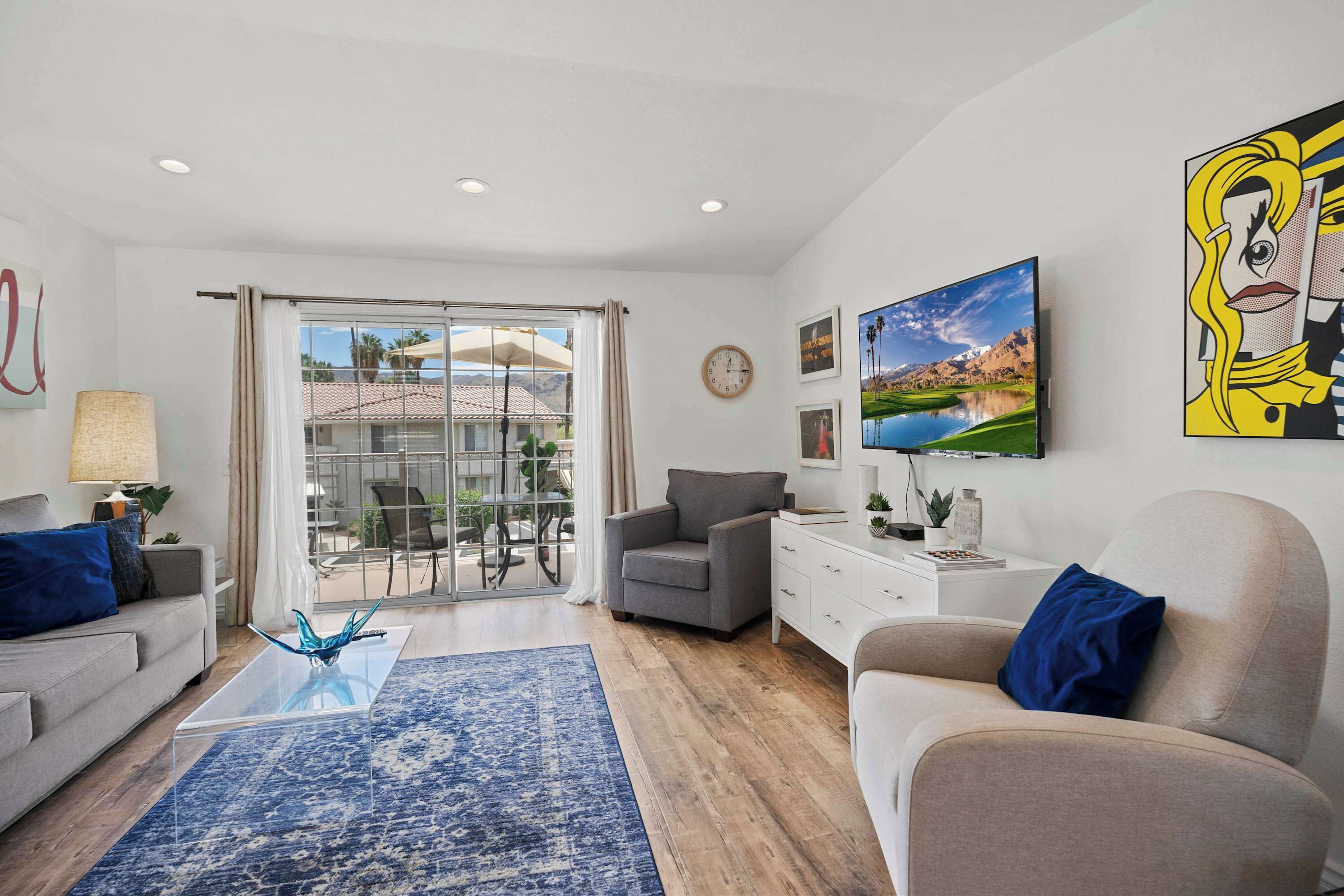Un salon moderne comprenant un canapé, un fauteuil, une table basse et donnant sur une terrasse extérieure grâce à une porte vitrée.