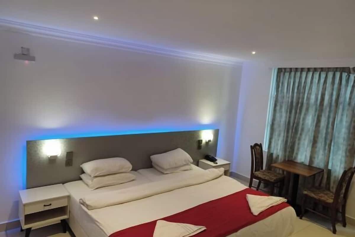 Een hotelkamer met een bed, nachtkastje, lamp en een eettafel met stoelen.