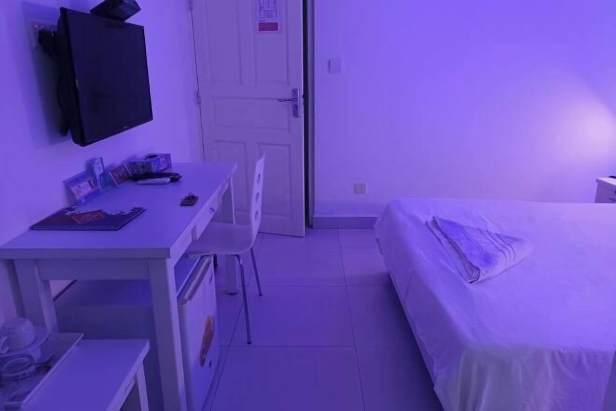 Een kamer met een bed, een bureau, een stoel, een aan de muur bevestigde televisie en een deur.