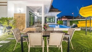 An outdoor patio with a dining table and chairs, a pool, and a yellow slide. - Villa me & you2 (Cha-am)