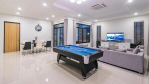 A modern living room with a pool table, a sofa, a TV, and a dining area. - Villa me & you2 (Cha-am)