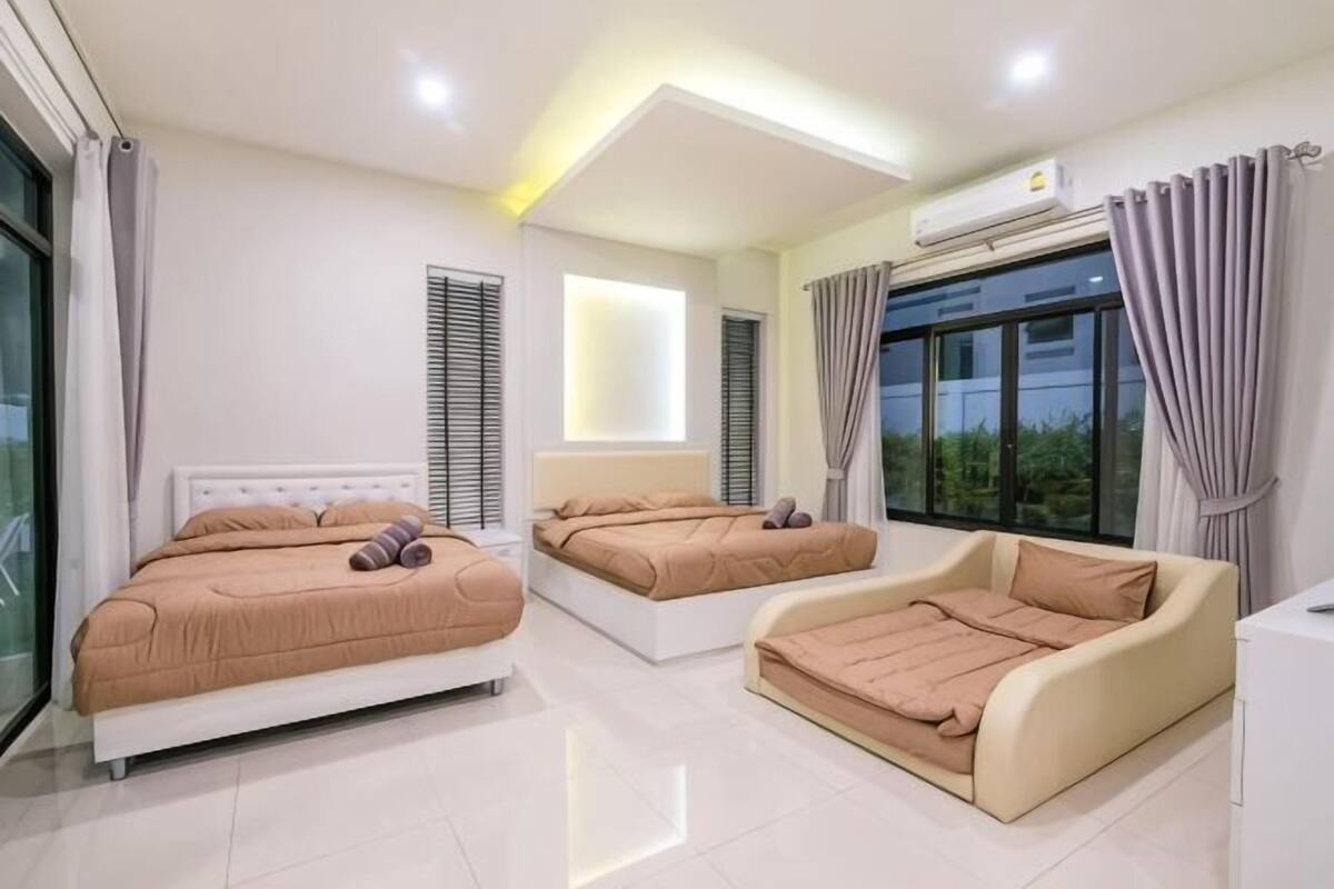 A modern bedroom with two beds, a sofa, and a large window.