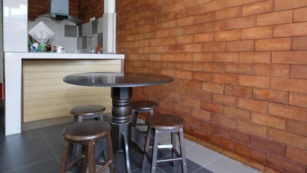 Una cocina con una mesa redonda y taburetes, un muro de ladrillo y una encimera blanca con diversos objetos.
