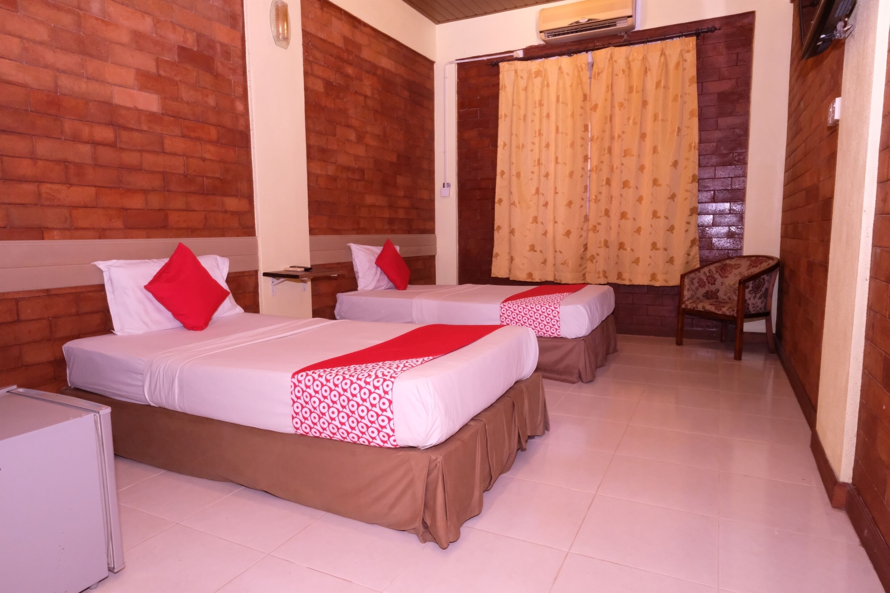 A hotel room with two beds, each with a red and white bedspread, a small table, and a chair.