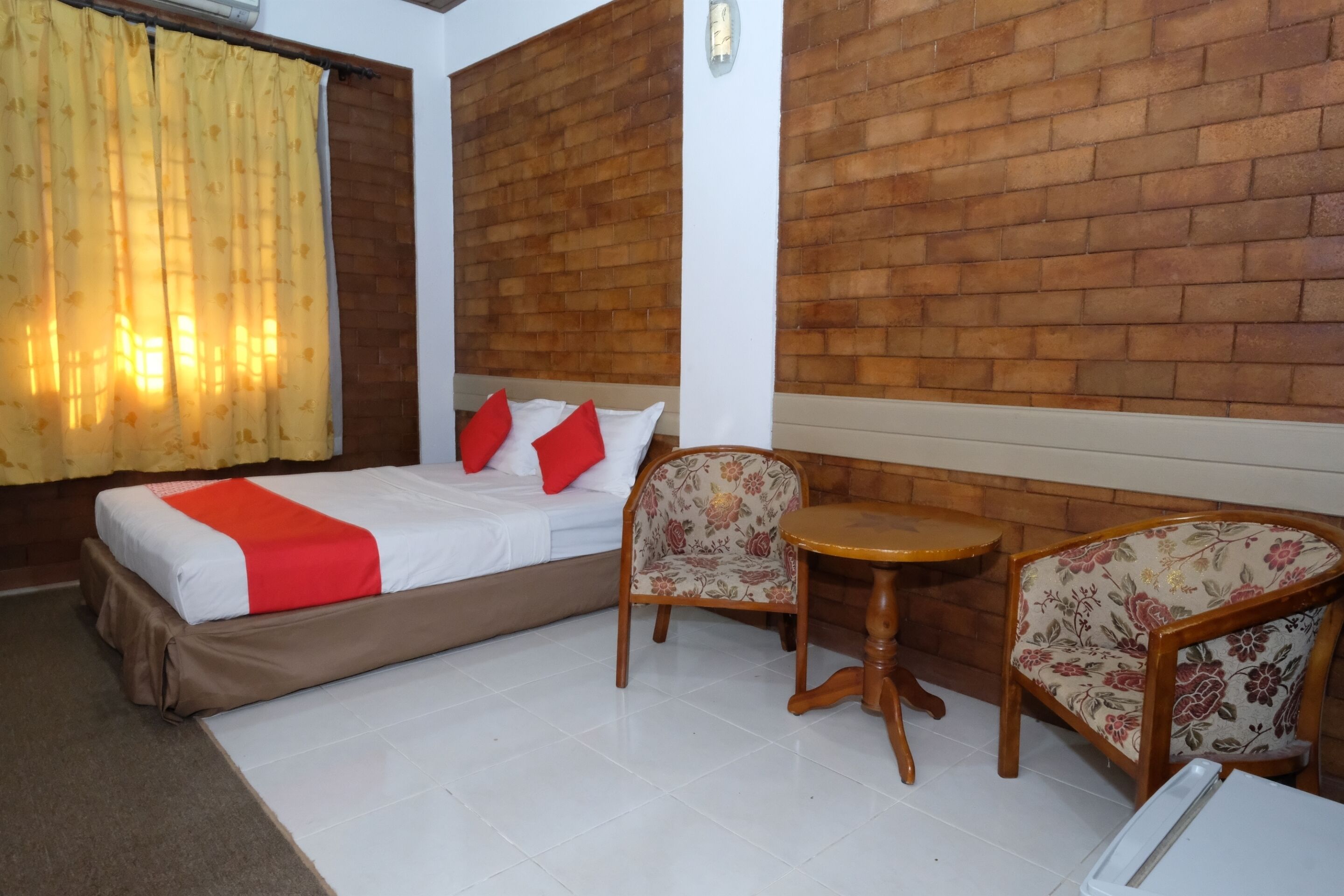 Quarto de hotel com uma cama, duas cadeiras, uma mesa pequena e uma parede de tijolos.