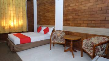 Quarto de hotel com uma cama, duas cadeiras, uma mesa pequena e uma parede de tijolos.