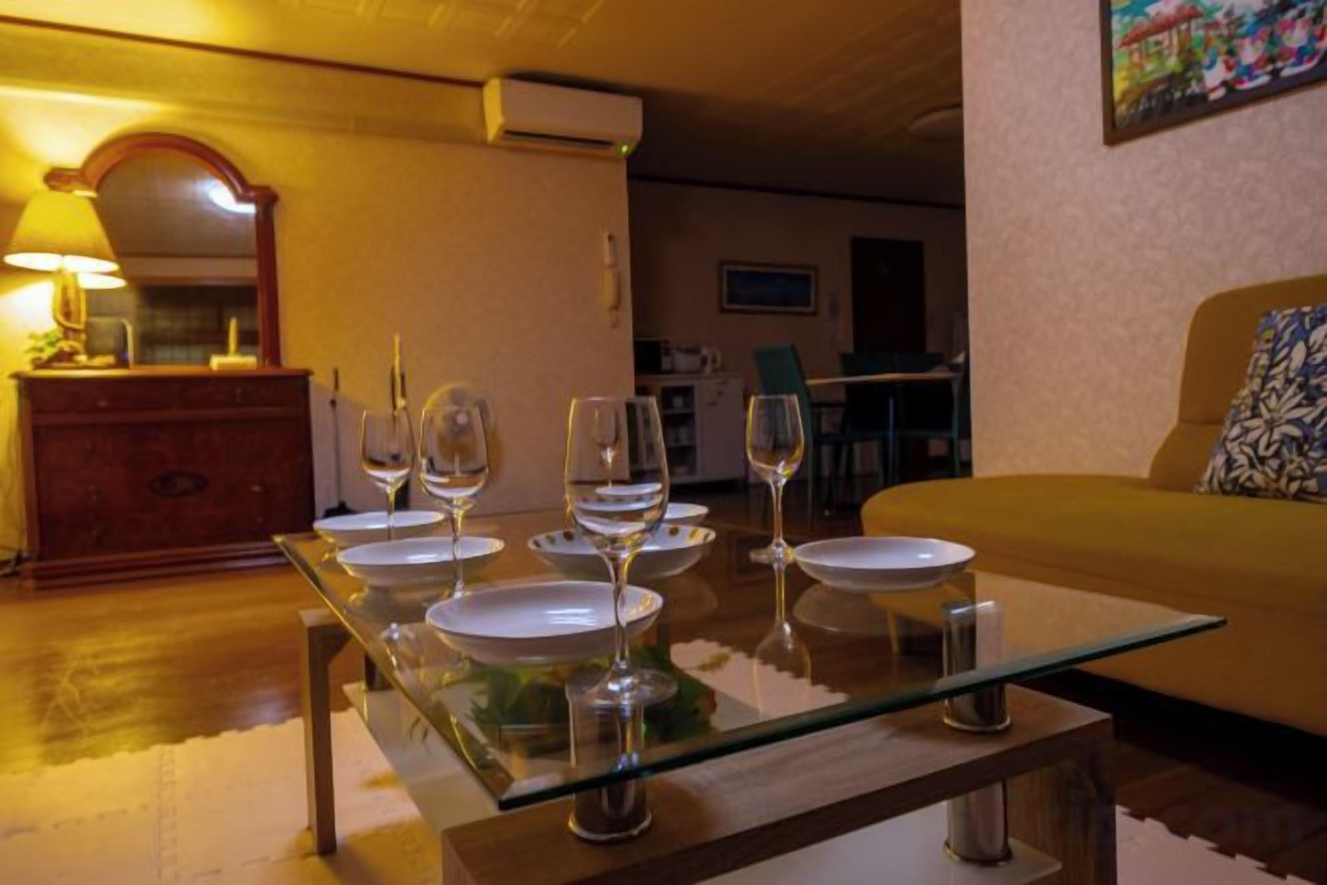 A dining area with a glass table set for four, a sofa, and a lamp.