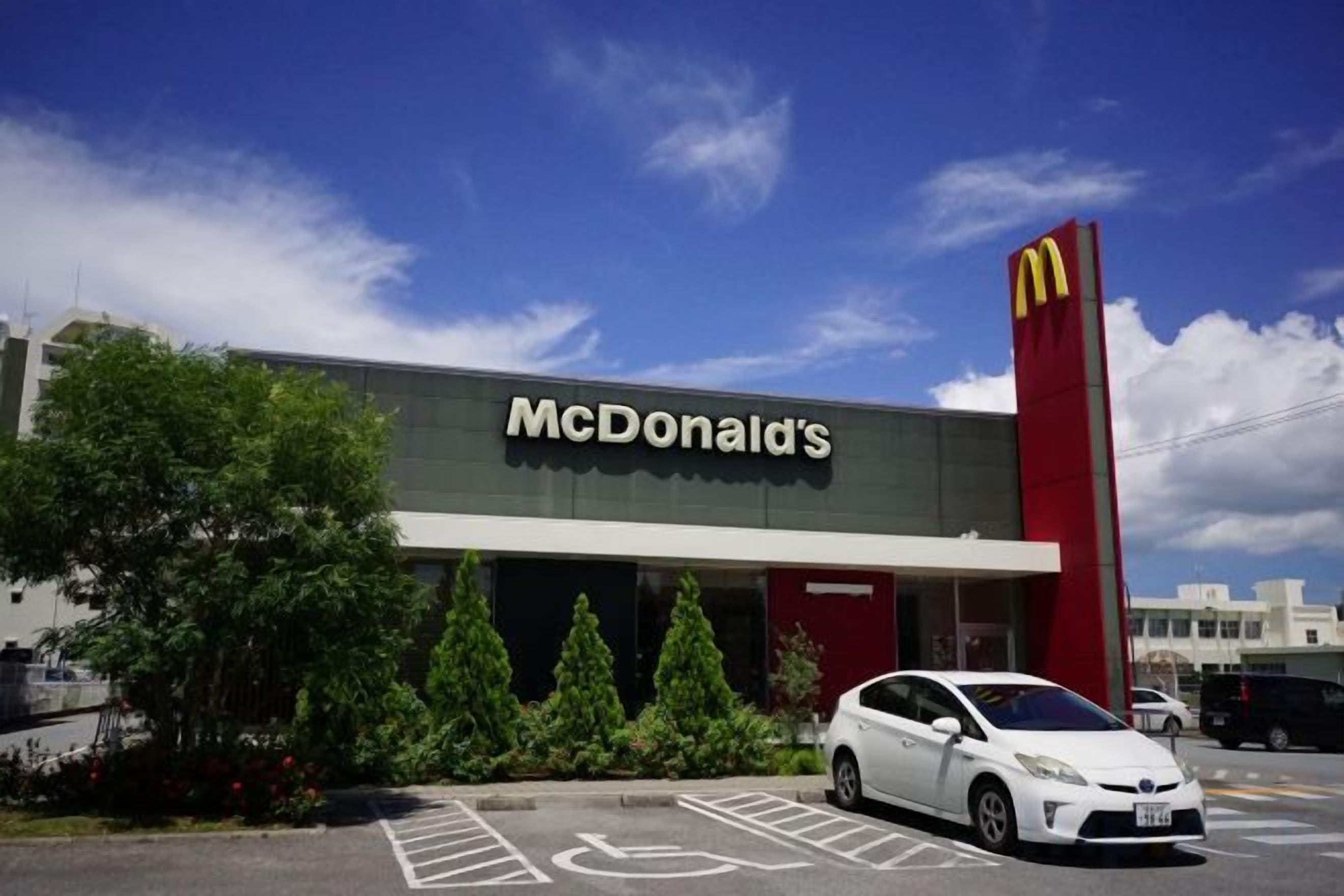 A McDonald's restaurant with a parking lot and a white car parked in front.