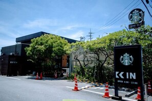 A Starbucks sign with a drive-thru service, a modern building, and traffic cones indicating construction or maintenance. - wing mihama (Chatan)