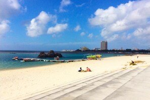 A beach with clear blue water, a pier, and a few people relaxing. - wing mihama (Chatan)