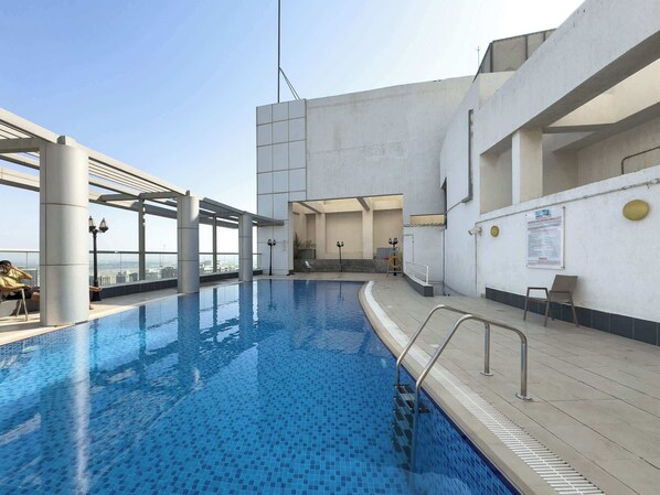 A rooftop swimming pool with clear blue water, a metal pool ladder, and a view of the cityscape.