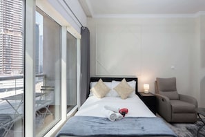 A hotel room with a bed, a chair, a nightstand, and a view of a building through a large window.
