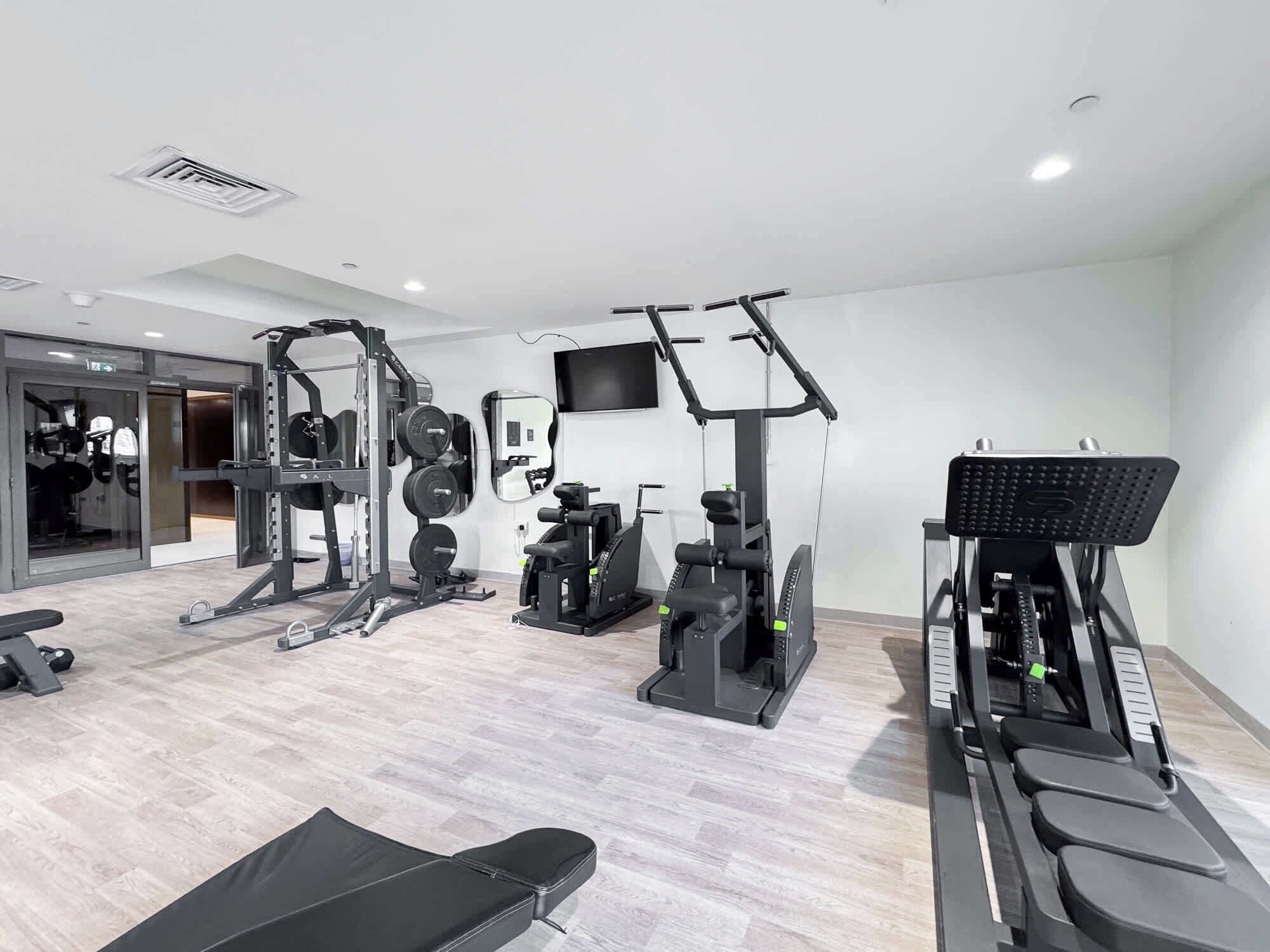 Ett modernt gym med olika typer av träningsutrustning, inklusive en bänk, styrketräningsmaskiner och ett löpband.