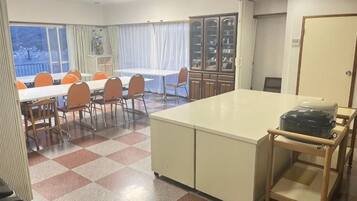 A hotel room with a checkered floor, a dining table with chairs, a small kitchen area, and a view through the window.