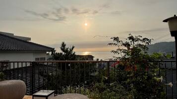 A balcony with a view of the sunset over the sea, surrounded by greenery and a fence.